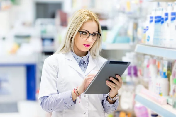 Detalles de la farmacia - médico rubio en uniforme blanco usando tableta y tecnología en el campo farmacéutico o médico —  Fotos de Stock