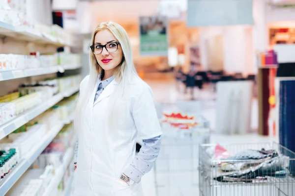 Επαγγελματική γυναικεία φαρμακοποιός στέκεται σε φαρμακείο phamarcy και χαμογελαστός. Λεπτομέρειες της φαρμακευτικής βιομηχανίας — Φωτογραφία Αρχείου