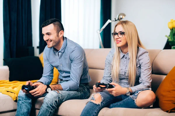 Νεαρό ζευγάρι παίζει ηλεκτρονικά παιχνίδια και τα βιντεοπαιχνίδια στην κονσόλα ενώ κάθεστε στον καναπέ στο νέο σπίτι — Φωτογραφία Αρχείου