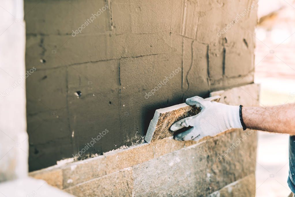 Construction worker mason closely placing stone tile on vertical wall. Industry details - construction site