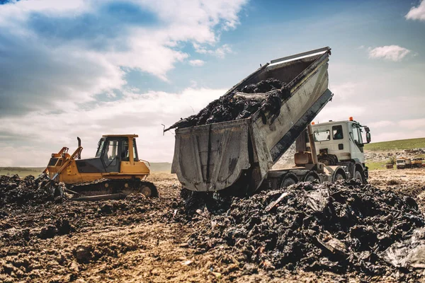 Dumping vrachtwagen lossen vuilnis op dumping site. Industriële bulldozer en graafmachine dumping vrachtwagens werken — Stockfoto