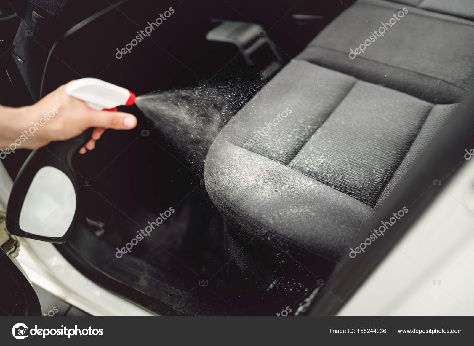 Car care concept, detailing and cleaning car interiors. Worker spraying cleaning solution on car
