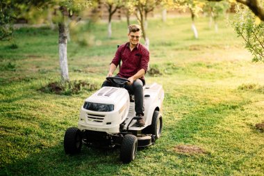 Man using ride on lawnmower, male riding lawn tractor and relaxing during sunset golden hour clipart