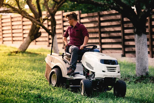 Gardner siega césped del patio trasero con vehículo motorizado. Detalles del paisaje —  Fotos de Stock