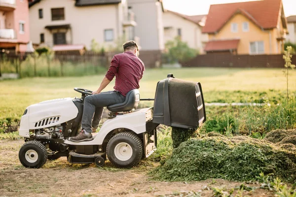 Professionele gardner lossen gemaaid gras van containter. Werknemer gebruik te maken van instrumenten voor landschapsarchitectuur — Stockfoto