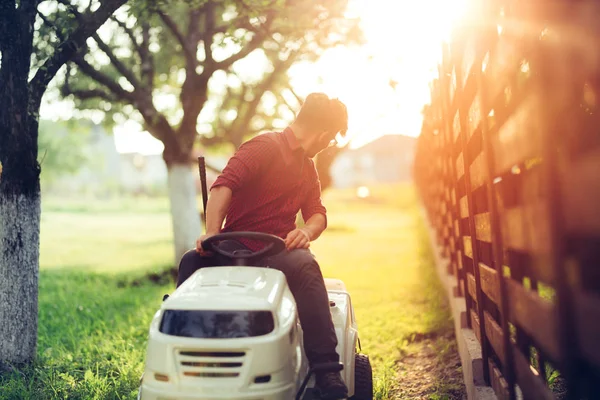 Detalles de jardinería durante la hora del atardecer. Hombre trabajando en cortadora de césped de paseo —  Fotos de Stock