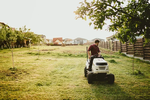 Efecto vintage de las obras de paisajismo. Trabajador masculino montando un cortador de césped tractor — Foto de Stock