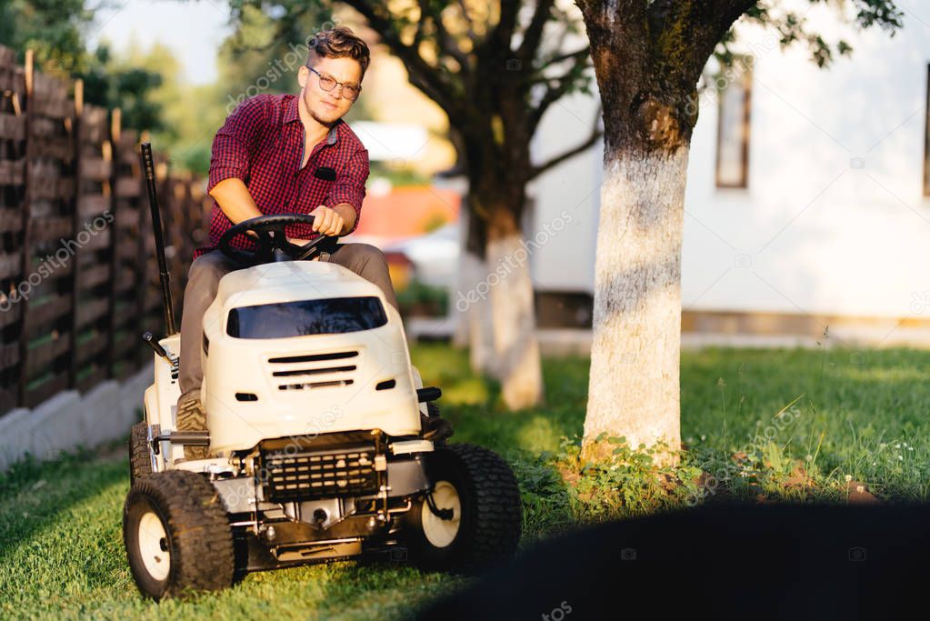 Portrait of man using lawn tractor and cutting grass in garden during weekend time