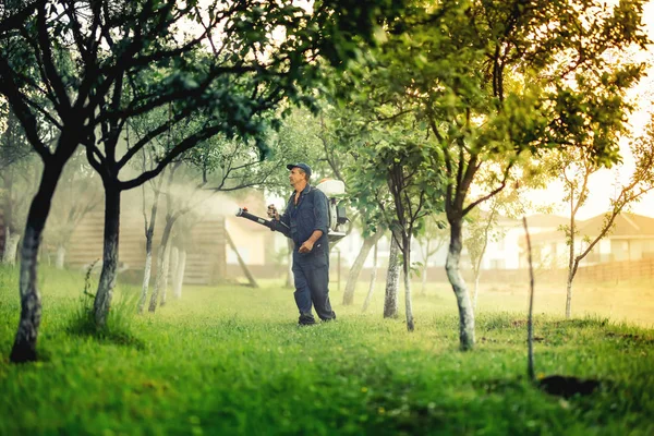 Industrial worker using mistblower for toxic pesticide distribution in fruit orchard — Stock Photo, Image