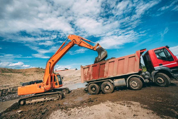 Máquinas pesadas que trabalham no estaleiro de construção - escavadeira carregando caminhões basculantes durante obras na estrada — Fotografia de Stock