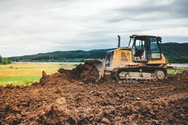 Mini excavadora amarilla nivelando la tierra para el sitio de fundación de la carretera — Foto de Stock