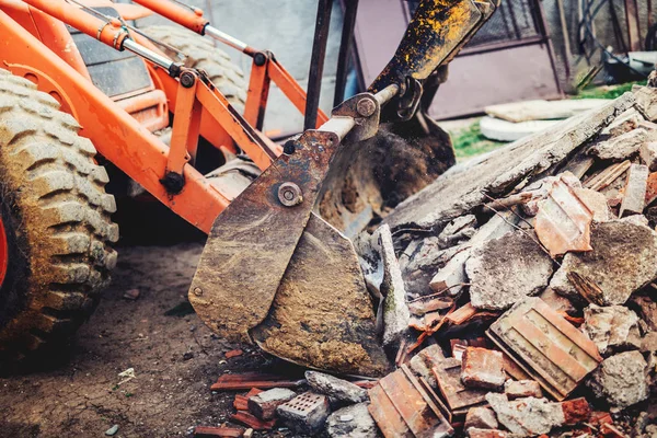 bulldozer demolishing concrete brick walls of small building and gathering debri, loading into dumper trucks