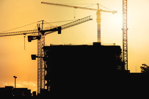 Industriella byggarbetsplatsen vid solnedgången med silhuetter av tornkranar — Stockfoto