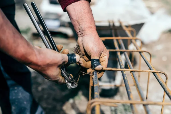 Mãos do trabalhador usando fio de aço e pinças para fixar barras de aço, preparando-se para derramamento de concreto na construção industrial sentar — Fotografia de Stock