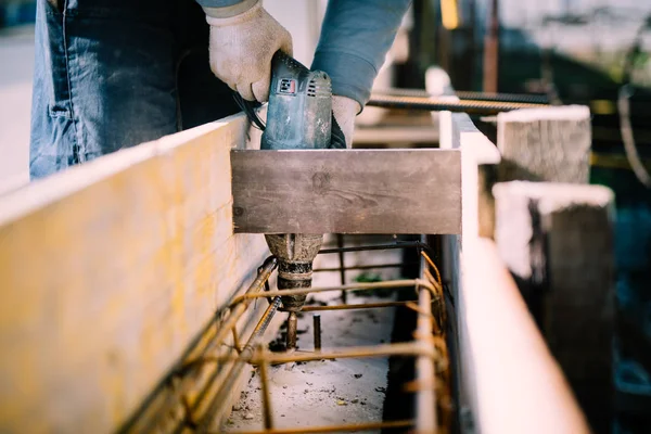 Trabalhador usando uma ferramenta elétrica de perfuração no canteiro de obras e criando furos no cimento para reforço de fundação — Fotografia de Stock