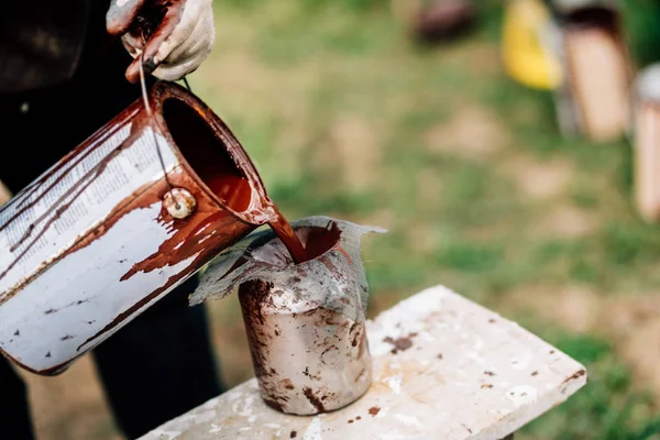 Construction worker wearing protective gloves pouring liquid paint into spray gun for painting wooden pieces — Stock Photo, Image