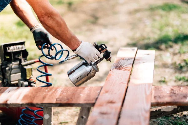 Arbeiter benutzt Spritzpistole zum Bemalen von braunem Holz — Stockfoto