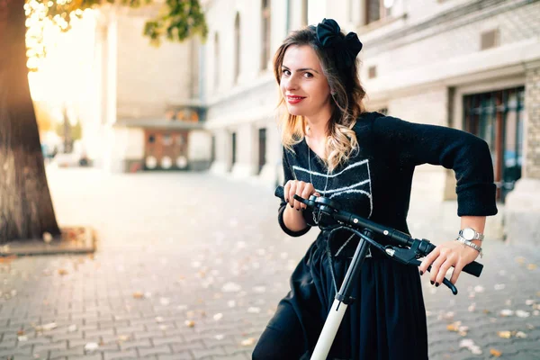 Donna sorridente con scossa elettrica scooter in una bella giornata autunnale godendo il tramonto. Ritratto di ragazza che utilizza la tecnologia come mezzo di trasporto — Foto Stock