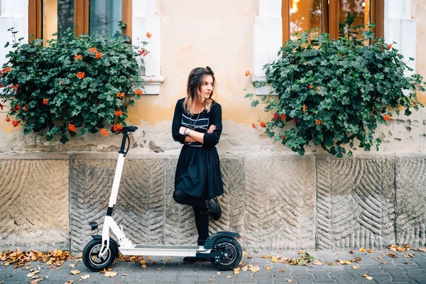 Detalhes de estilo de vida moderno, menina feliz com flores na cidade urbana apreciando o scooter elétrico. Felicidade e conceito despreocupado — Fotografia de Stock