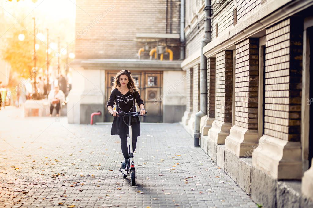 Trendy woman, beautiful brunette girl riding electric scooter in modern city