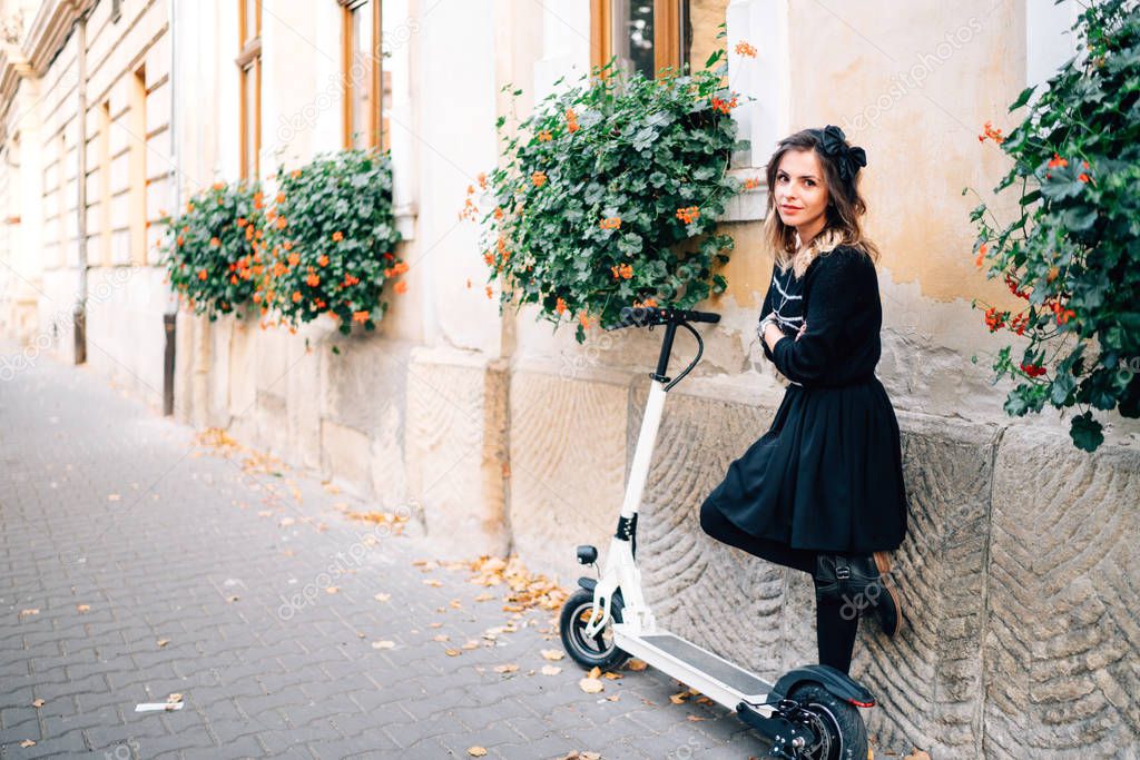 urban lifestyle details - happy woman standing on an alley with flowers and electric kick scooter