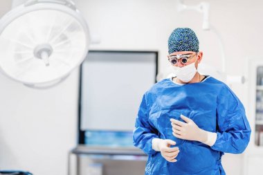 Ameliyathane cerrah portresi. Estetik Plastik Cerrahi önlük, gözlük ve ameliyat için hazırlanıyor eldiven giyiyor