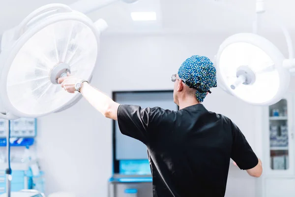 Mužské chirurg se chystá na operaci, upevnění svítilny a úprava světla v operační místnosti — Stock fotografie
