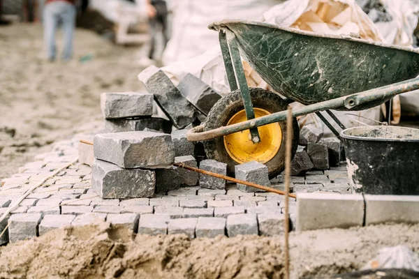 Pavimento de pavimentação detalhes com pedras de granito, blocos de paralelepípedos e carrinho de mão no local de construção — Fotografia de Stock