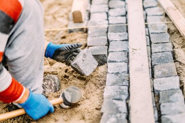 Close up details of construction works with industrial worker placing granite cobblestone blocks on path or alley clipart
