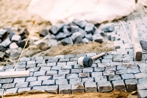 Строительная площадка, инструменты и детали, монтаж тротуаров и скал. Гранитные камни, лежащие на песке, изготовление тротуара — стоковое фото