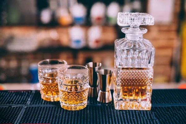 Close up of whiskey bottle, crystal glasses and cocktail tools in modern bar, on counter — Stock Photo, Image