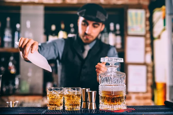 Close up of elengant bartender pouring whiskey and ice on fresh cocktails in modern bar — Stock Photo, Image