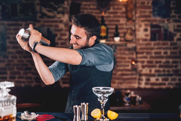 Lächelnder Barmann mit Shaker zur Cocktailzubereitung. Porträt eines Barmanns, der Margarita auf Tequila-Basis in einer lokalen Kneipe zubereitet — Stockfoto