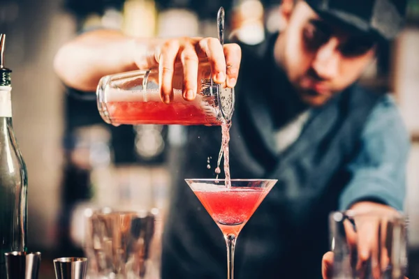 Barman preparando e derramando coquetel vermelho na classe martini. coquetel cosmopolita com fundo bar — Fotografia de Stock