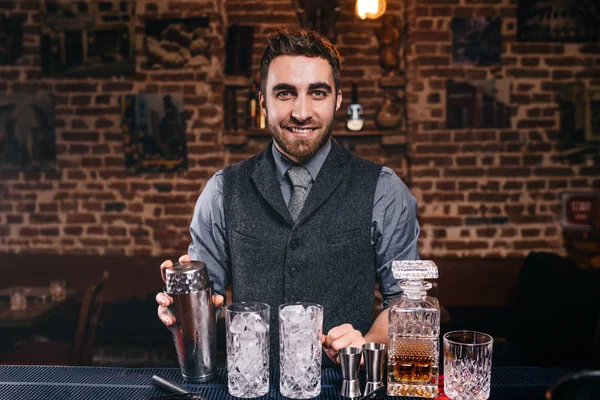 Barman uśmiecha się do kamery podczas przygotowywania drinków w barze. Napoje alkoholowe i profesjonalny barman — Zdjęcie stockowe