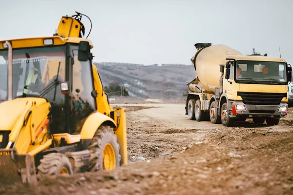 Industrial backhoe excavator machinery and cement truck on road construction site — Stock Photo, Image