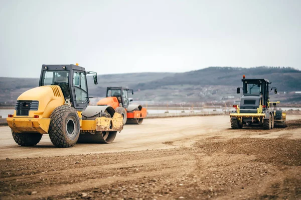 Compactadores de suelo vibratorio en el sitio de construcción de carreteras. Trabajos de carretera industriales con maquinaria pesada — Foto de Stock