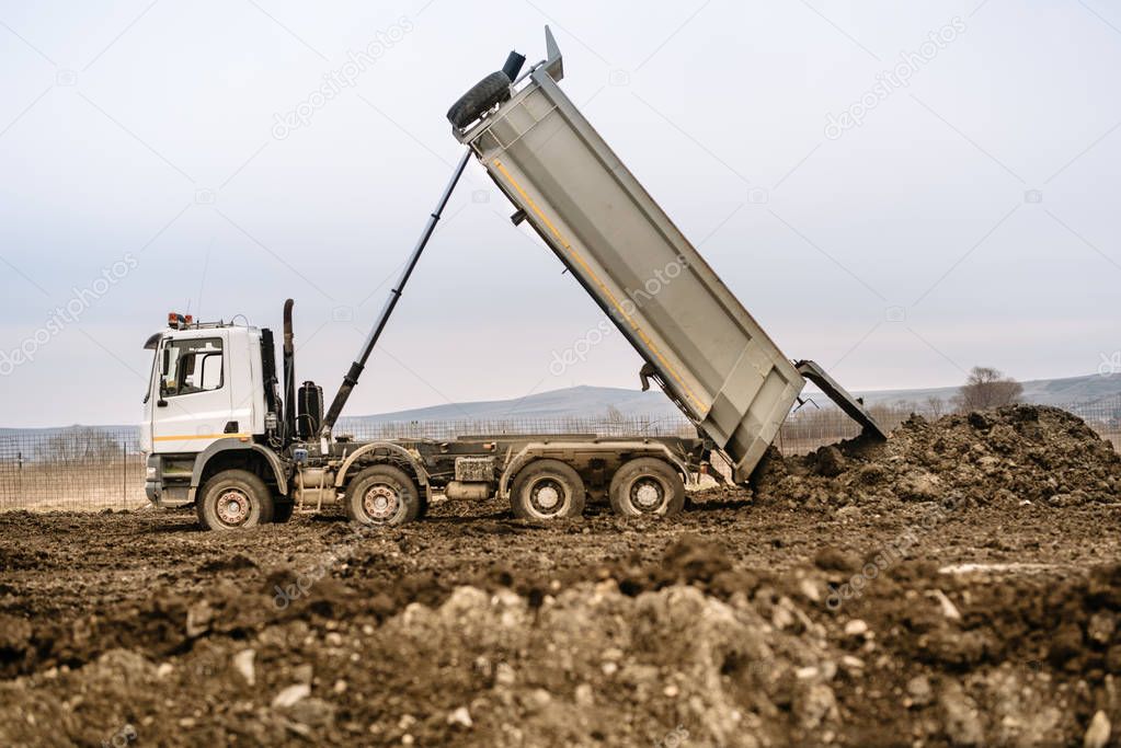 Industrial dumper truck un loading gravel and earth at highway construction site