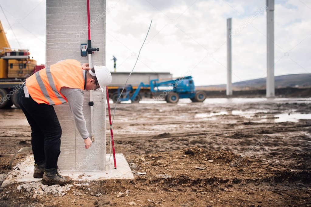 industrial engineer working on building site with cement pillars and surveying tools