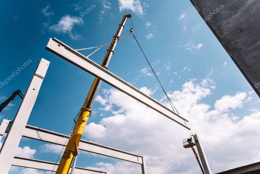 Industrial cranes operating and working on construction site moving cement beams and pillars