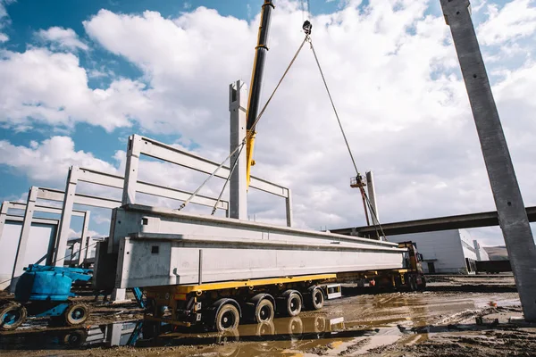 Industrial crane unloading prefabricated cement pillars from cargo — Stock Photo, Image