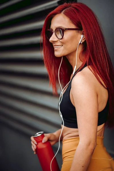 Bela mulher sorrindo, ouvindo música e água potável durante o treino — Fotografia de Stock