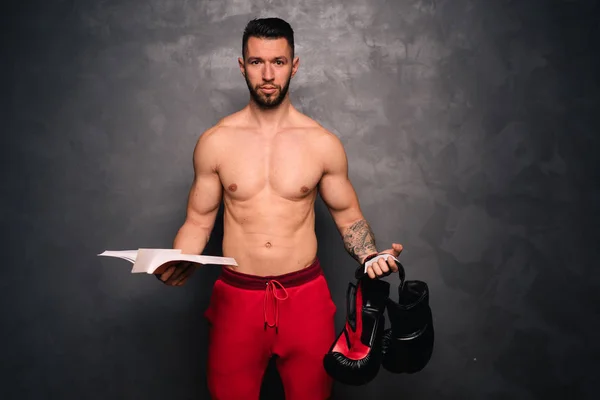 Portrait of attractive muscular caucasian man holding sports items and books, promoting a healthy lifestyle — Stock Photo, Image