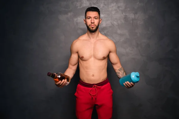 Υγιεινός τρόπος ζωής έννοια - πορτρέτο του γυμνόστηθη μυϊκή καυκάσιος άνδρας κρατώντας ένα μπουκάλι αλκοόλ και ένα μπουκάλι νερό — Φωτογραφία Αρχείου