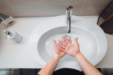 Güzel bir kadın ellerini sabun ve dezenfektanla dikkatlice yıkıyor. Üst görünüm, hijyen detayları. 