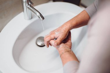 Evde sabun ve su kullanan yaşlı bir kadın.