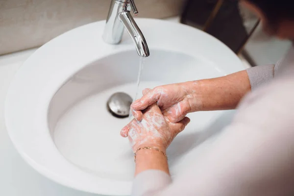 elderly woman carefully washing hands with soap and sanitiser in bathroom. top view, details of hygiene, disinfecting hands