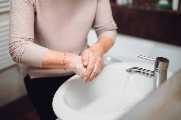 elderly woman carefully washing hands with soap and sanitiser in home bathroom. top view, details of hygiene, disinfecting hands