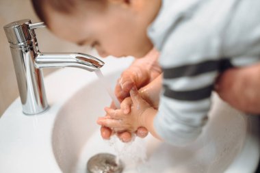 . Baba ve çocuk ellerini temizlemek için sabun ve musluk suyu kullanıyor. Baba oğul lavaboda el yıkıyorlar.