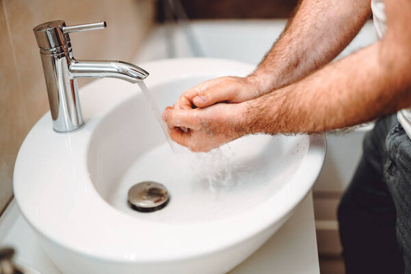 Young male adult washing hands at home using disinfectant and soap, tap water and cleaning cosmetics